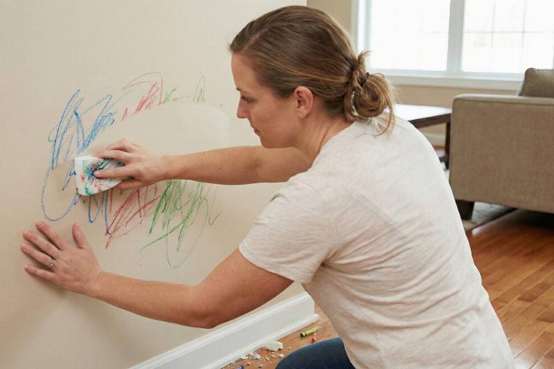 A woman using a magic eraser to remove crayon marks from a wall. 