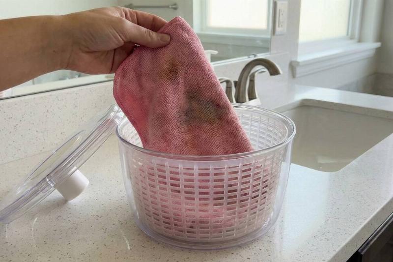 A hand putting a reusable makeup towel in a salad spinner.