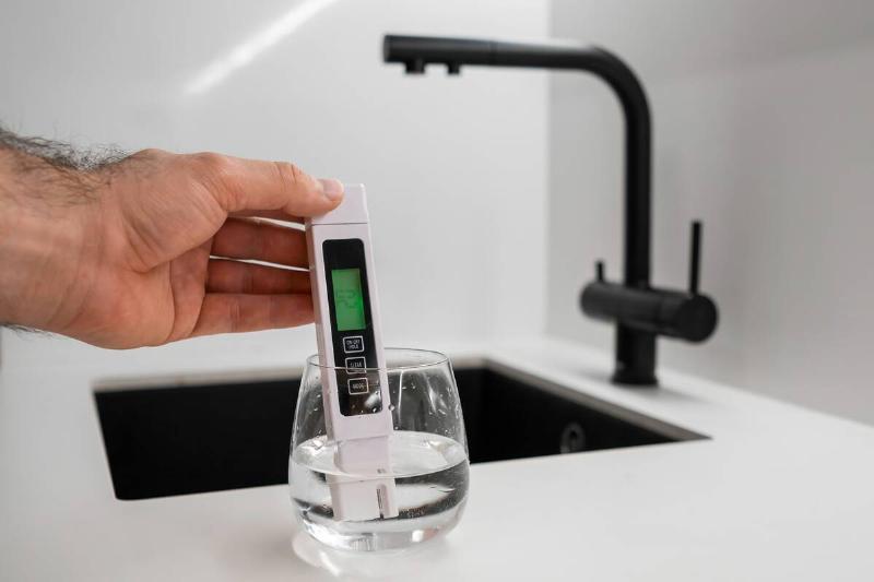 Man hand immerses TDS tester or conductometer into the water in glass.