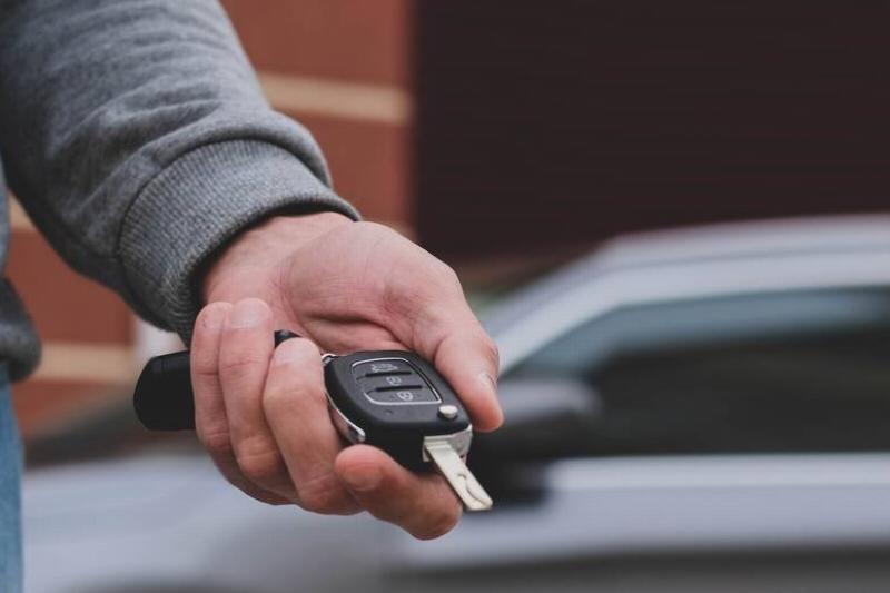 мужчина-перед-новой-машиной-и-держит-ключи-2026-01-07-06-04-34-utc Рука, держащая ключ от машины с брелоком.