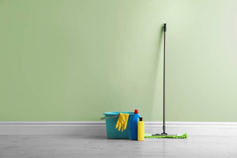 Mop and cleaning supplies on floor near green wall indoors.