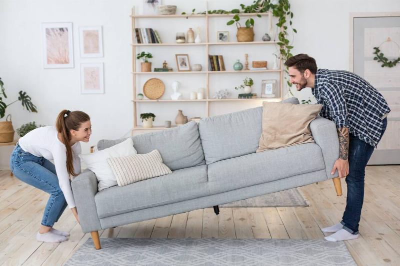 Man and woman moving couch in living room. 