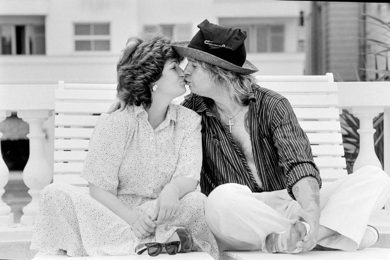 Ozzy and Sharon Osbourne sitting on a bench, kissing each other