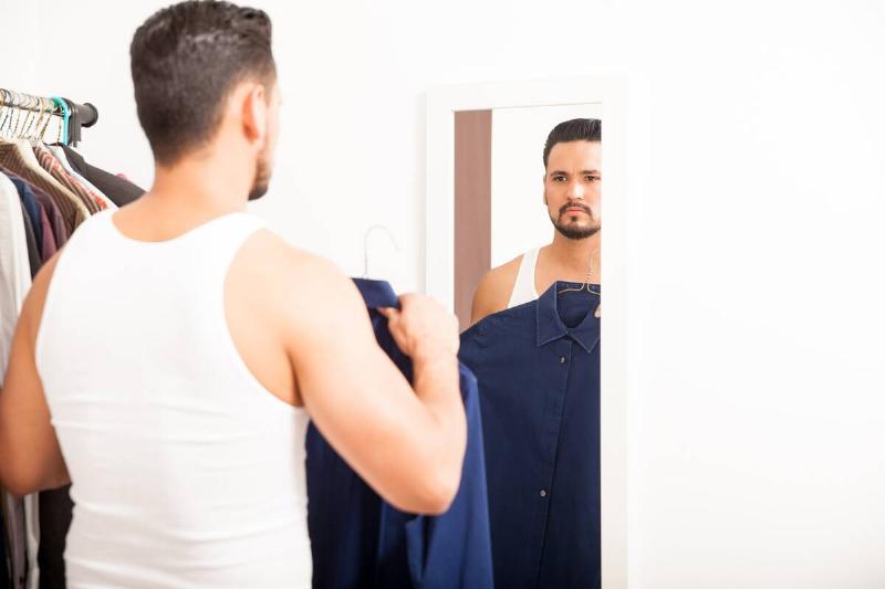 Man looking at shirt while dressing in the mirror. 