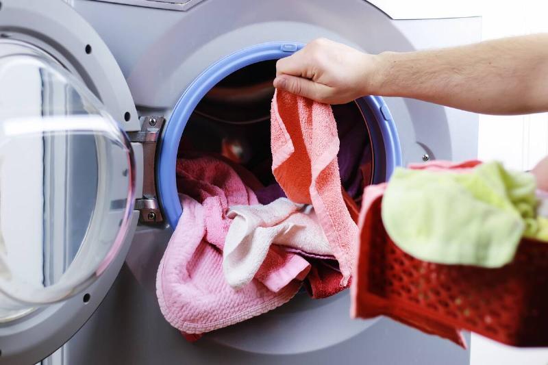 Hands putting dirty cloths in the washing machine. 