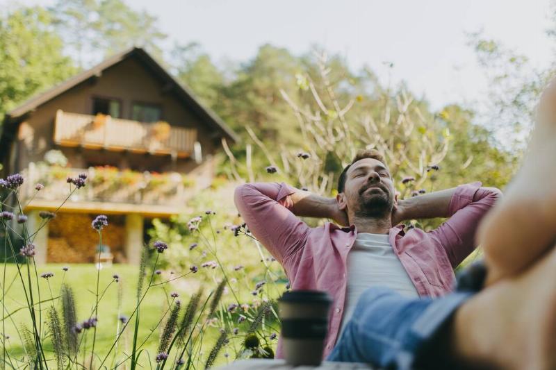 расслабленный-мужчина-сидит-в-саду-с-ногими-на вкладке-2026-01-05-06-20-34-utc Мужчина отдыхает у себя во дворе.