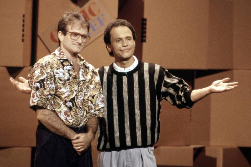 Robin Williams and Billy Crystal standing together in front of a wall of cardboard boxes