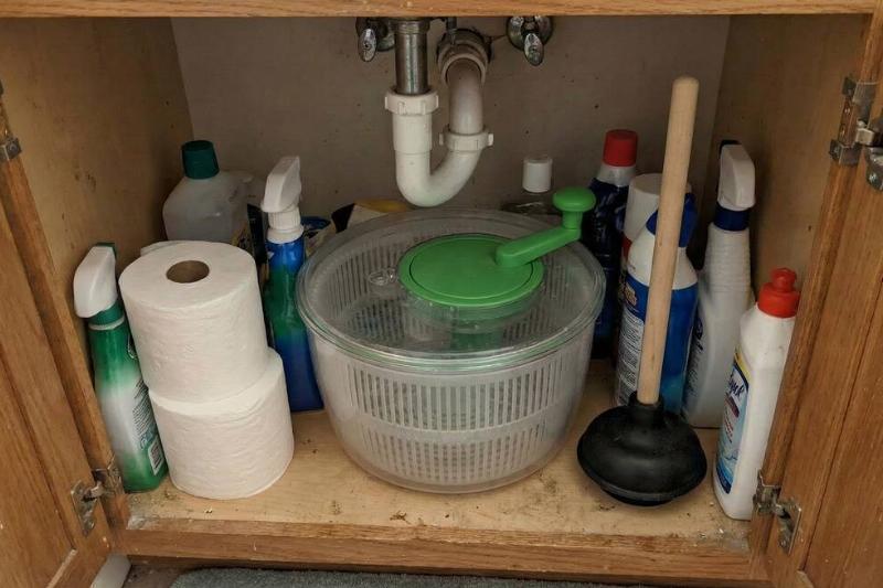 A salad spinner being stored under a bathroom sink.
