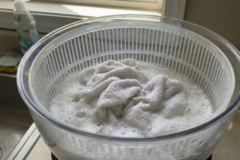 A salad spinner with a hand towel in it that has been used as a washing machine. 