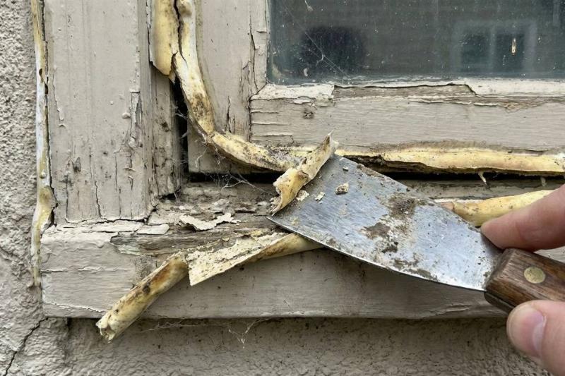 A scraper tool removing old caulk from a window frame