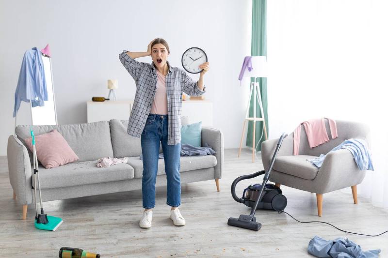 Shocked lady holding a clock in a messy room. 
