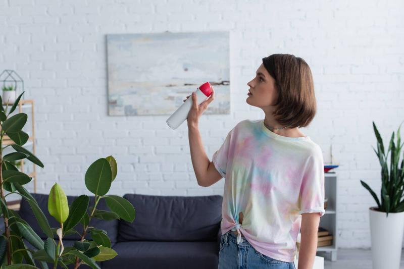 Side view of woman spraying air freshener in a living room.