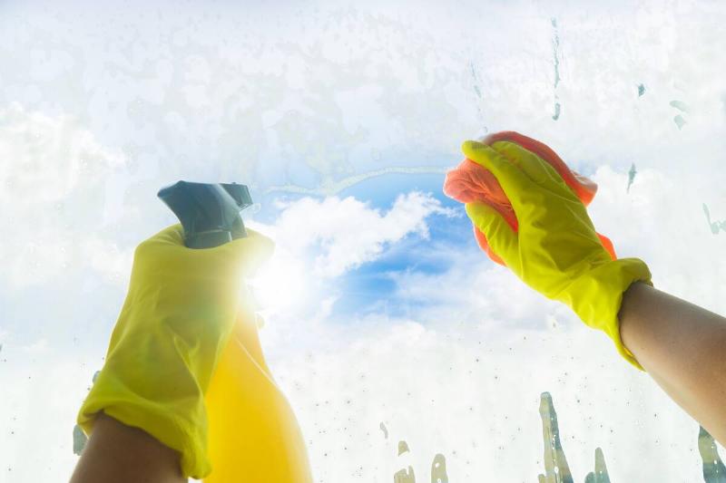 Someones hands in yellow gloves cleaning a window on a sunny day.