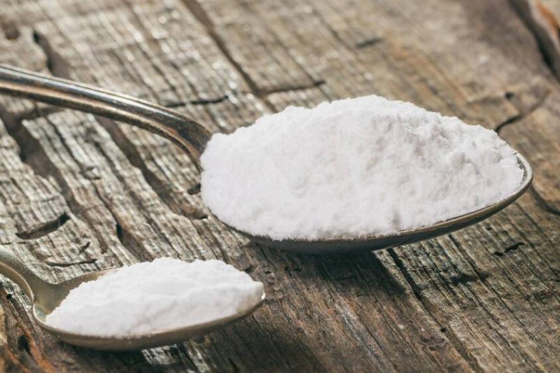 Tablespoon and teaspoon with baking soda, on wooden surface.