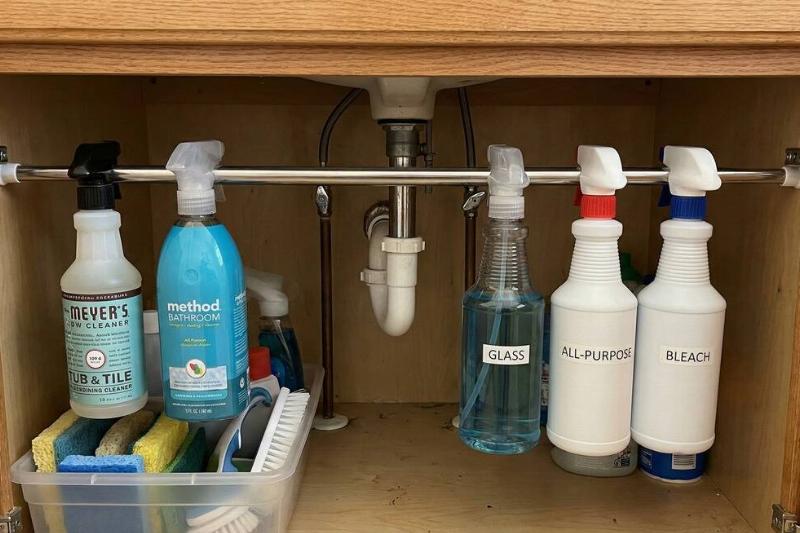 Spray bottles of cleaners hanging under a sink on a tension rod. 