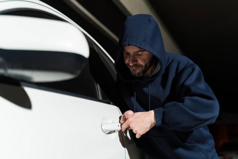 Thief in hoodie trying to unlock car door at night. 