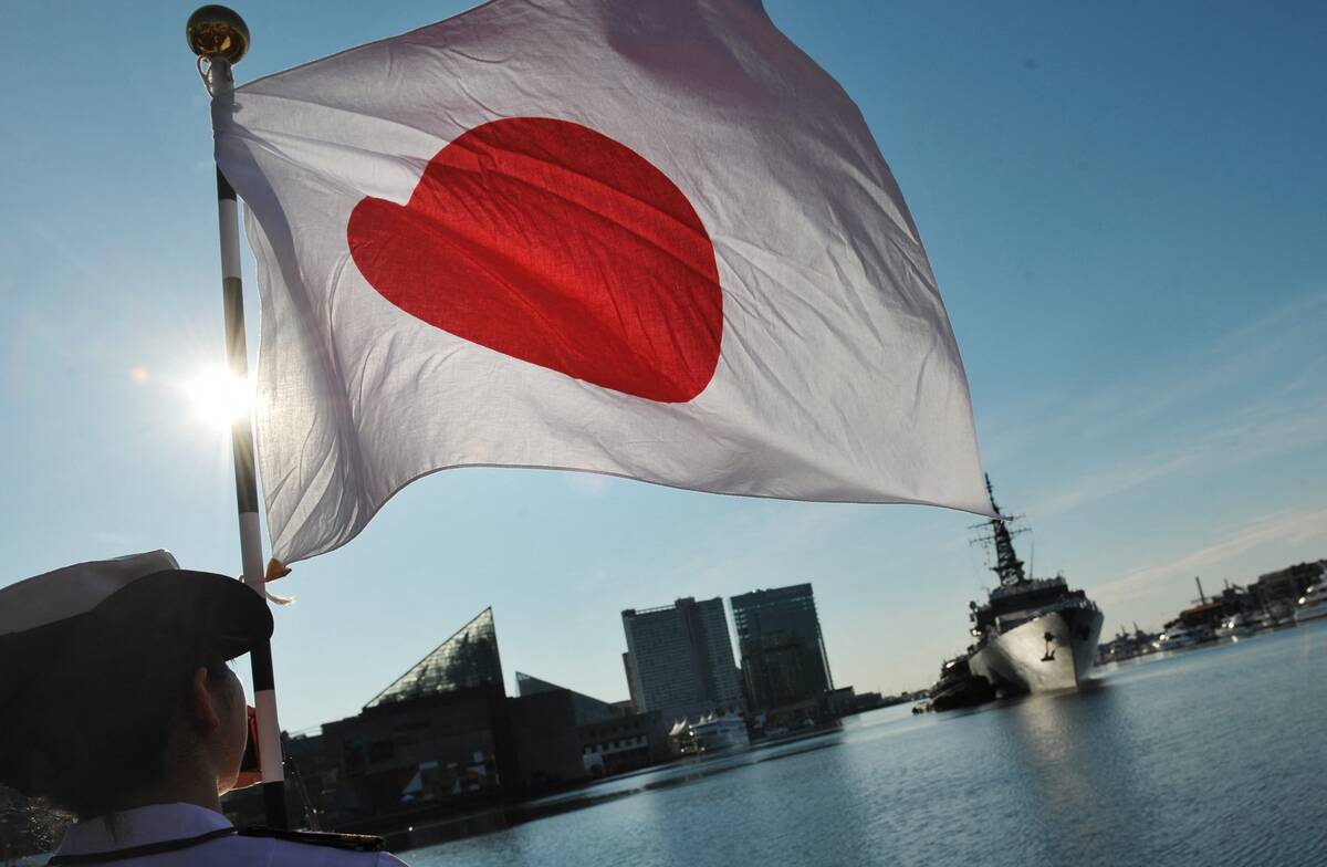 Member of the Japan Maritime Self-Defence Force (JMSDF) holding the Japanese flag by the water