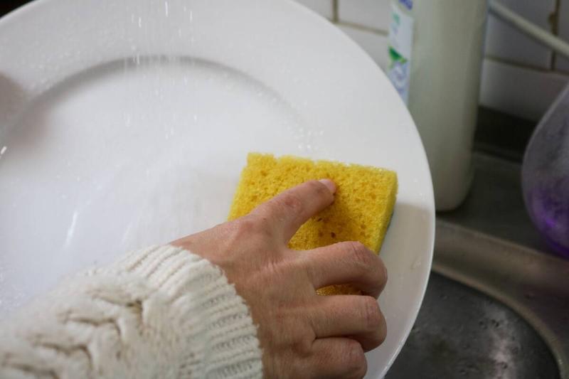 Hand washing dishes with sponge. 