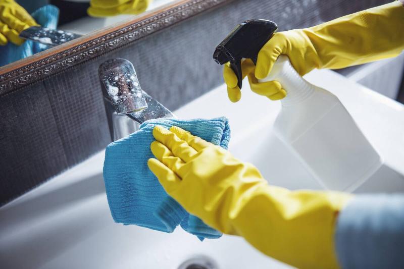 Hands in gloves cleaning bathroom tap. 