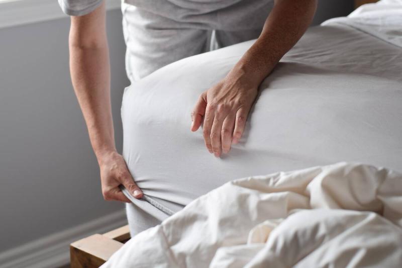 Hands putting fitted sheet on a bed. 