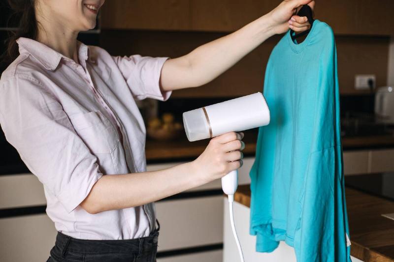 A woman holding a hair dryer and using it to get wrinkles out of a shirt. 