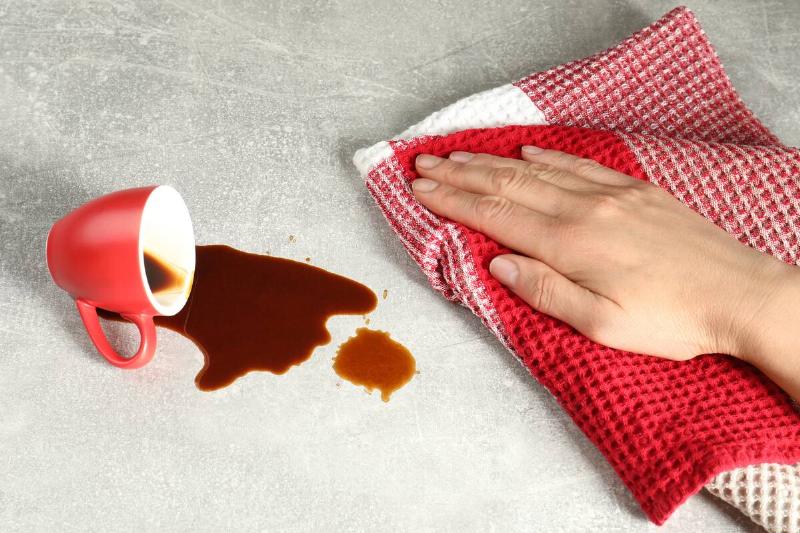 Woman wiping spilled coffee on grey table.