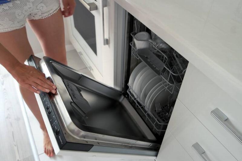 Hands wiping dishwasher door seal.