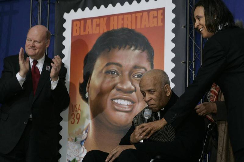 People standing and sitting around an enlarged USPS stamp featuring Hattie McDaniel's image