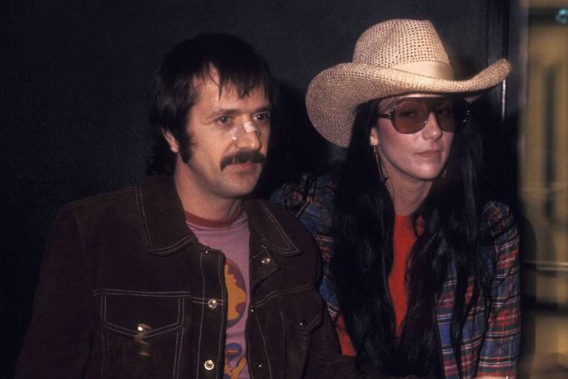 Sonny Bono and Cher standing together in a dark room