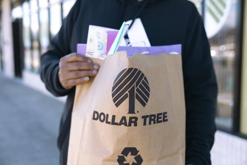 A customer carries a paper shopping bag outside a Dollar Tree store.