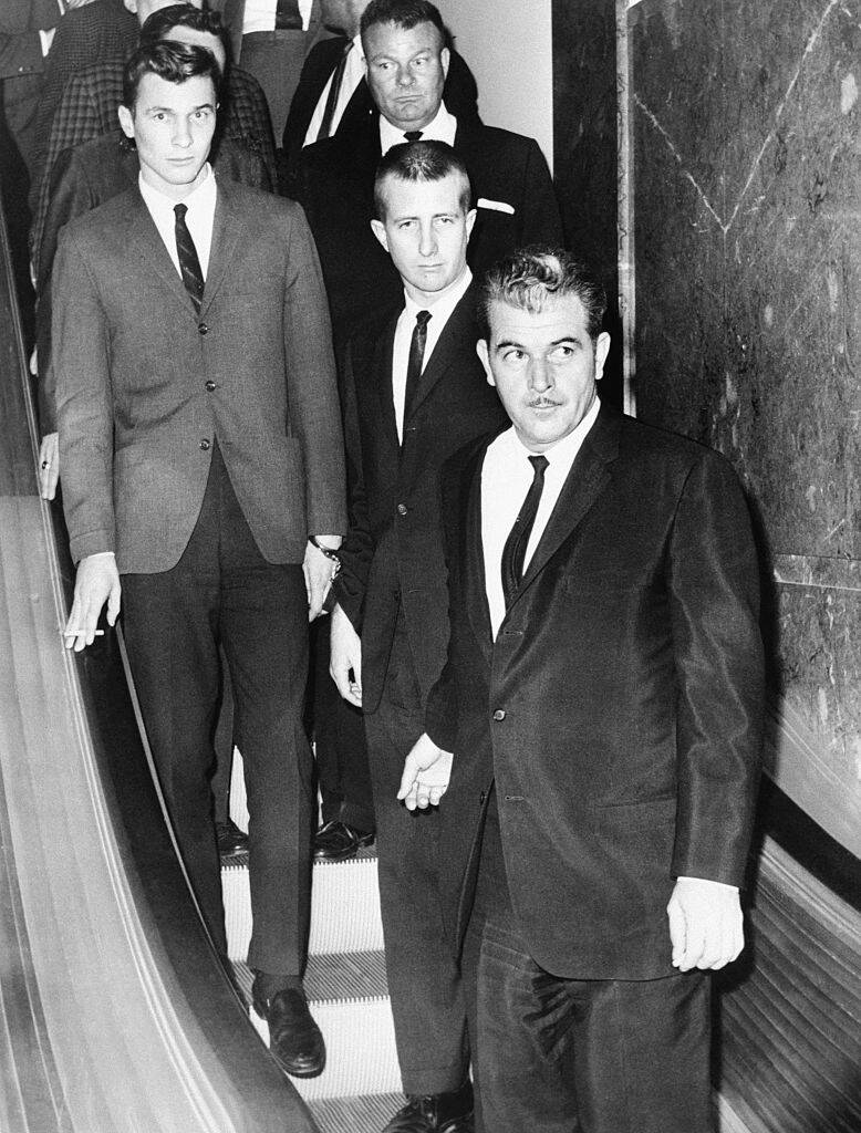Joe Amsler, Barry Keenan and John Irwin being led down an escalator by a group of men