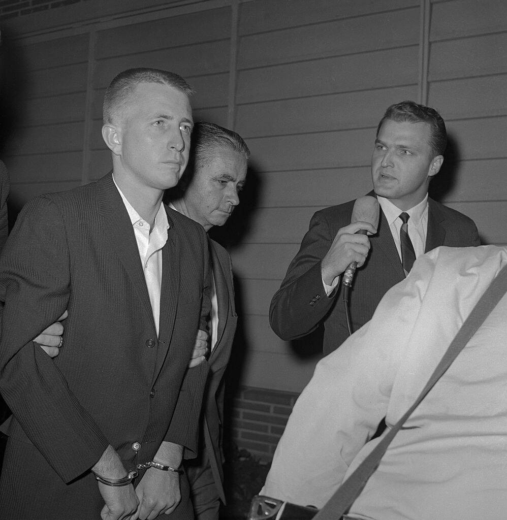 Man leading Barry Keenan, who's in handcuffs, along the outside of a building