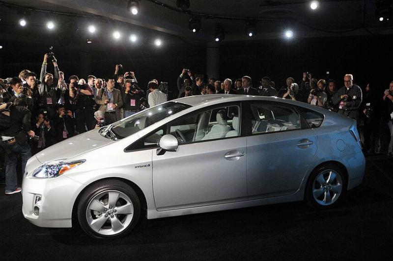 Photographers standing around a silver 2010 Toyota Prius