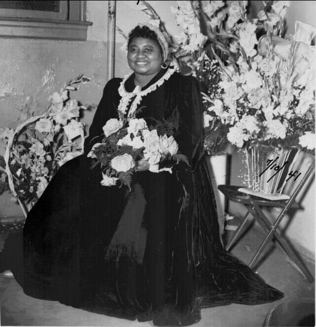 Hattie McDaniel sitting in a chair, holding and surrounded by flowers