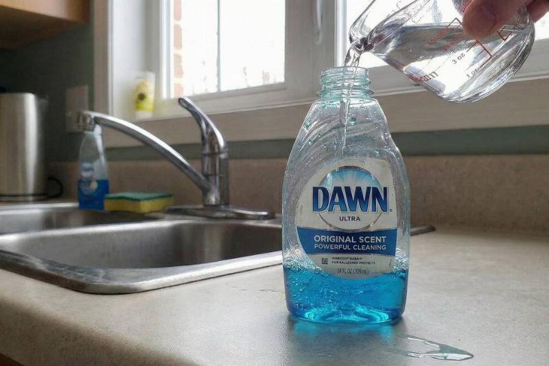 A hand pouring water into the dish soap bottle.