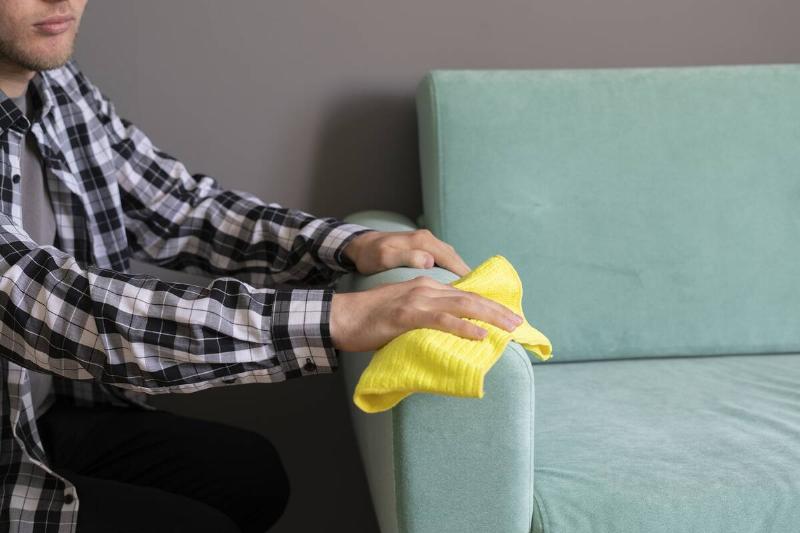 A worker cleaning the arm of a couch. 