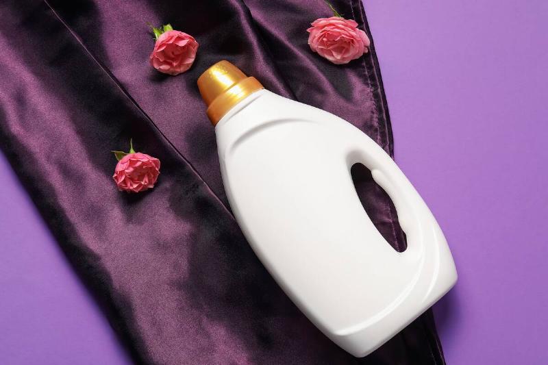 Bottle of fabric softener, flowers and color cloth on purple background.
