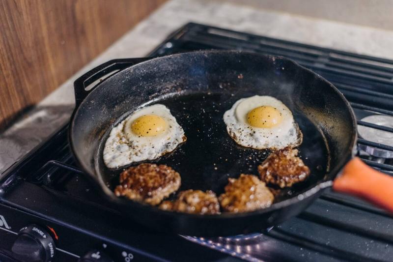 Eggs and bacon cooking in cast iron pan. 