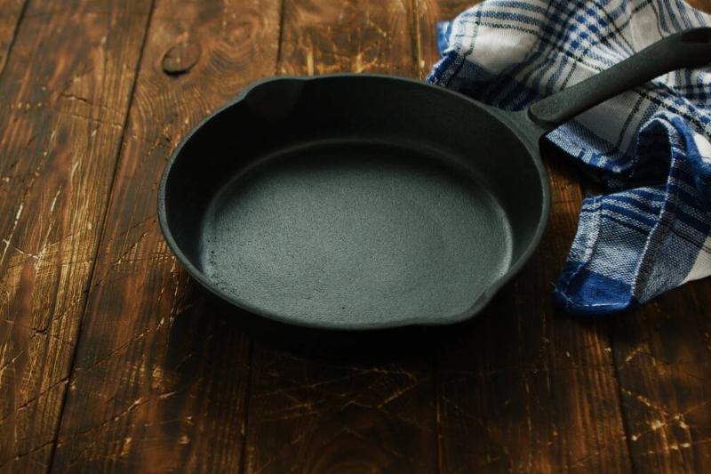 A dry cast iron pan with a cloth on a wood table. 