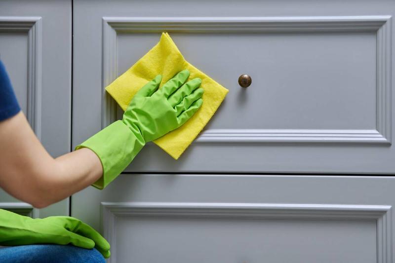 A hand holding a soft cloth to clean the front of a kitchen drawer. 