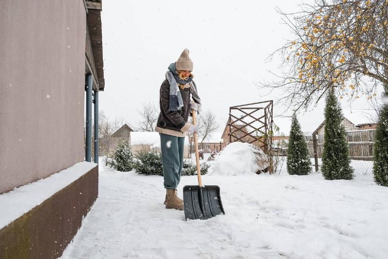 Close-up of a woman cleaning and clearing snow in front of the house on a sunny and frosty day.