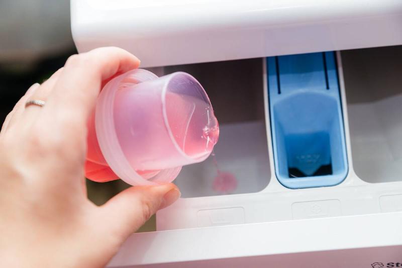 Close-up of a woman's hand pouring laundry detergent into the powder compartment of the washing machine.