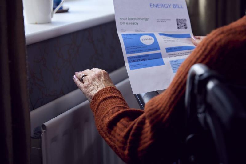 Woman feeling thermostat and reading energy bill. 