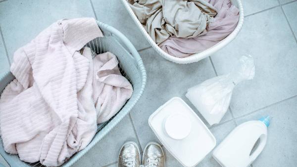Two baskets of dirty clothes and laundry detergent on the ground. 