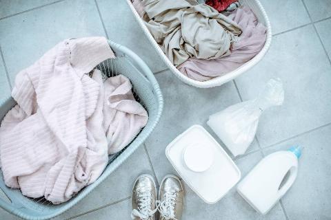 Two baskets of dirty clothes and laundry detergent on the ground. 