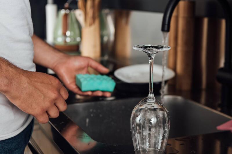 A man washing a glass wine glass in a sink with a sponge. 
