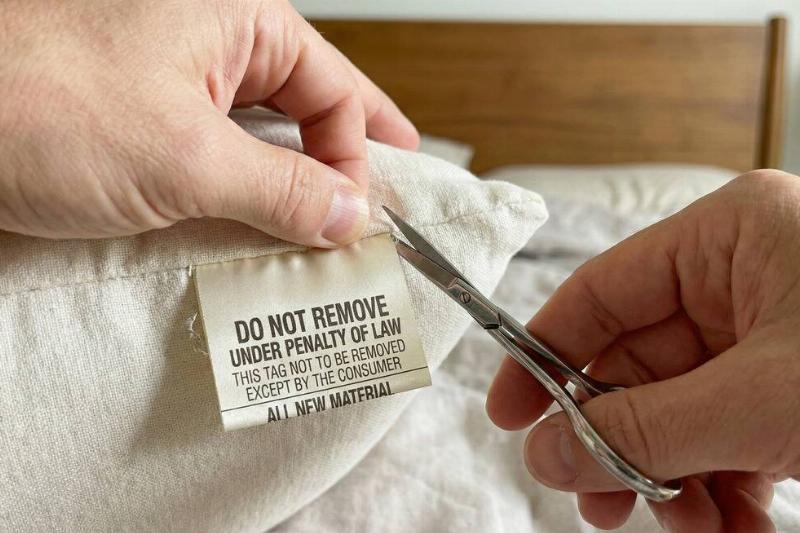 A person using scissors to cut a tag off of a pillow. 