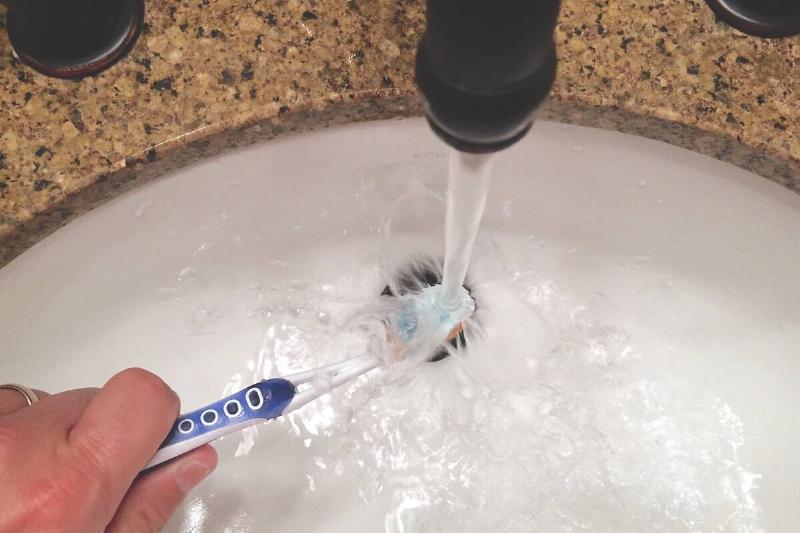 Rinsing toothbrush under bathroom sink.