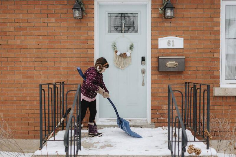 Girl shoveling snow on porch.