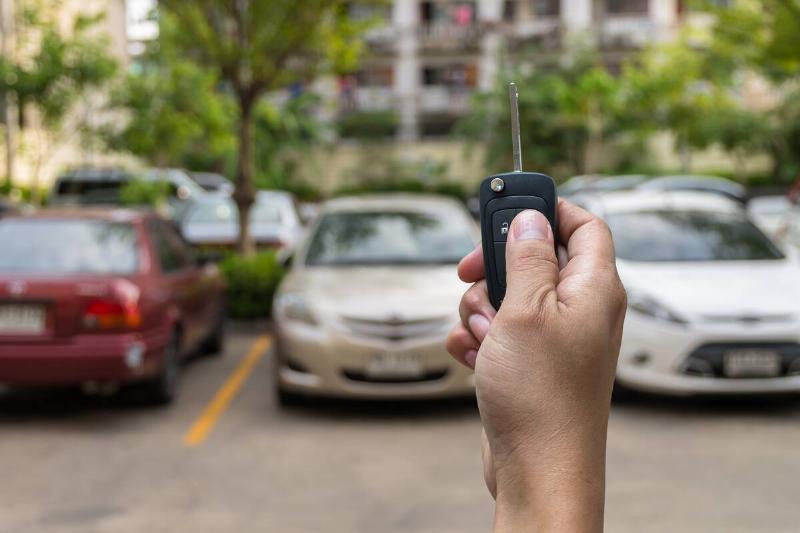 A hand holding a key fob in front of a parking lot. 
